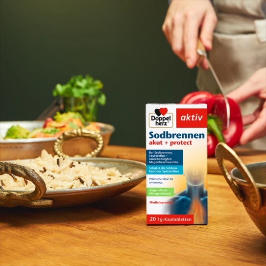 Doppelherz Sodbrennen akut + protect auf Küchentisch, Frau schneidet Paprika im Hintergrund
